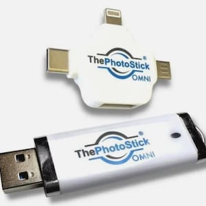 Op de afbeelding: Witte ThePhotoStick Omni USB-stick met een blauw cirkellogo en een witte USB-connector. De stick is verbonden met een witte adapter met een Lightning-connector, een USB-C-connector en een micro-USB-connector.