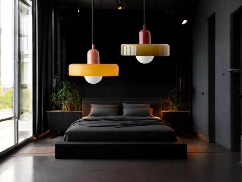 May include: Two modern pendant lights with yellow and brown shades hanging over a black bed in a dark room.