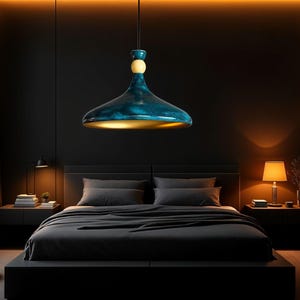Puede incluir: Una lámpara colgante de color azul oscuro con interior dorado cuelga sobre una cama con ropa de cama gris oscuro en un dormitorio moderno.