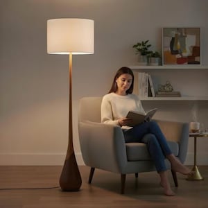 May include: A tall floor lamp with a slender wooden base and a cylindrical white fabric shade. The lamp features a teardrop-shaped bottom section made of dark wood that transitions into a thin, light-colored wooden stem supporting the light.