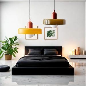 May include: A modern bedroom with a black platform bed, black bedding, and two yellow and brown pendant lights hanging from the ceiling. The room has a white wall, a large window, and a small plant in a brown pot.