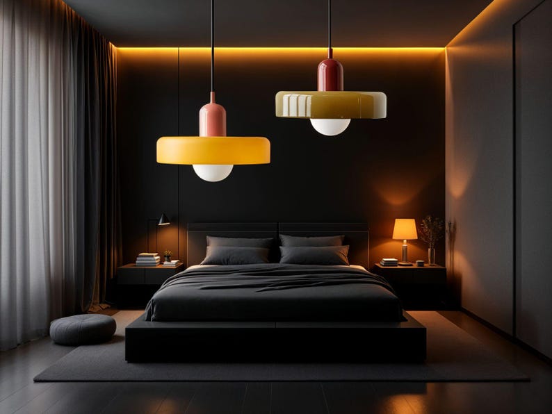 May include: Two modern pendant lights with yellow and red shades hang over a black bed in a dark bedroom.