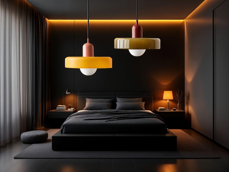 May include: Two modern pendant lights with yellow and red shades hang over a black bed with white bedding in a dark room.