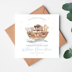 Pode incluir: Um cart&atilde;o de felicita&ccedil;&otilde;es quadrado branco com uma ilustra&ccedil;&atilde;o em aguarela de uma arca de madeira cheia de animais, incluindo elefantes e girafas. O texto diz TO A SPECIAL GODSON, with love on your CHRISTENING DAY, William Oliver Price e Sunday 10th August 2023.
