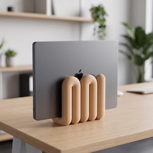 May include: A dark gray laptop with a visible Apple logo is held upright by a beige, U-shaped, multi-ribbed stand. The stand features a smooth, rounded, continuous form that supports the device in a vertical position on a wooden surface.
