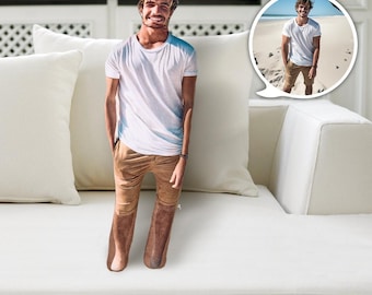 Könnte beinhalten: Eine Person in einem weißen T-Shirt und braunen Hosen steht auf einem weißen Sofa. Die Person lächelt und schaut in die Kamera. Im Hintergrund ist ein kleines Bild der Person am Strand zu sehen.