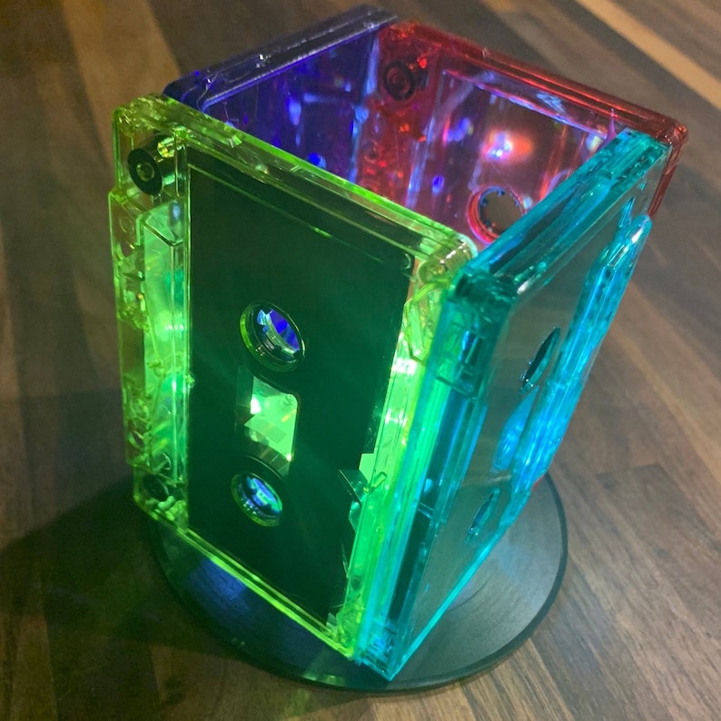 Peut inclure: Une pile de quatre cassettes audio transparentes, chacune d'une couleur diff&eacute;rente&nbsp;: vert, bleu, rouge et violet. Les cassettes sont empil&eacute;es les unes sur les autres, la cassette verte en bas et la cassette violette en haut.