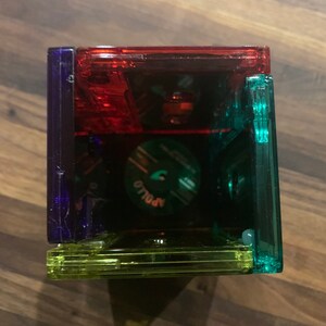 Peut inclure: Une pile de quatre bo&icirc;tiers de cassettes en plastique transparent, chacun d'une couleur diff&eacute;rente&nbsp;: rouge, bleu, vert et jaune. Les bo&icirc;tiers sont empil&eacute;s les uns sur les autres, le rouge en haut et le jaune en bas. Les bo&icirc;tiers sont tous vides et l'&eacute;tiquette sur le bo&icirc;tier rouge indique "Apollo".