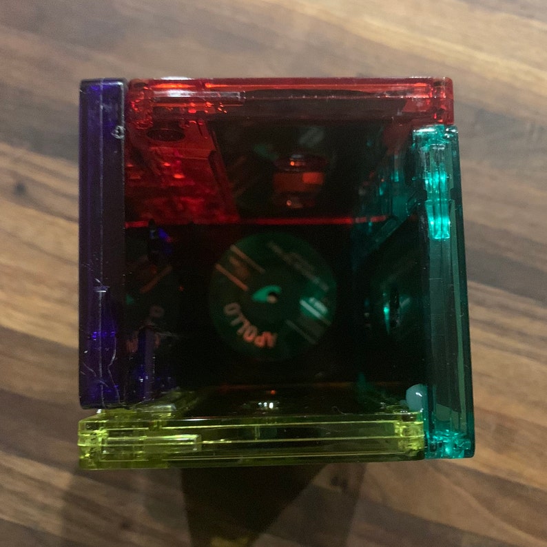 Peut inclure: Une pile de quatre bo&icirc;tiers de cassettes en plastique transparent, chacun d'une couleur diff&eacute;rente&nbsp;: rouge, bleu, vert et jaune. Les bo&icirc;tiers sont empil&eacute;s les uns sur les autres, le rouge en haut et le jaune en bas. Les bo&icirc;tiers sont tous vides et l'&eacute;tiquette sur le bo&icirc;tier rouge indique "Apollo".