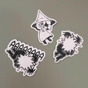 Puede incluir: Tres pegatinas en blanco y negro. Una muestra un personaje con sombrero y abrigo. Dos pegatinas representan figuras con un efecto de explosión, una con la palabra "AAAAAAA".