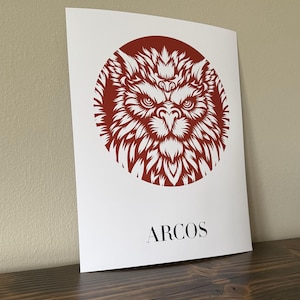 以下が含まれることがあります： 白いプリントに、赤い円の中に白いスタイリッシュな狼の顔のイラストが描かれています。円の真下に黒い文字で「ARCOS」と印刷されています。
