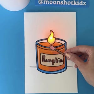 May include: A drawing of a pumpkin-scented candle with a lit flame. The candle is orange with a blue rim and the word "Pumpkin" is written on the front. A match is held near the flame. The background is blue.