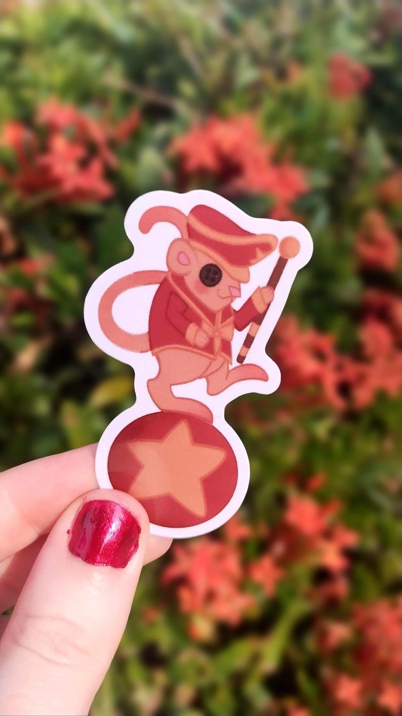 May include: A red and white sticker of a cartoon mouse wearing a red and gold uniform and a hat, balancing on a red ball with a yellow star. The mouse is holding a red and white striped stick.