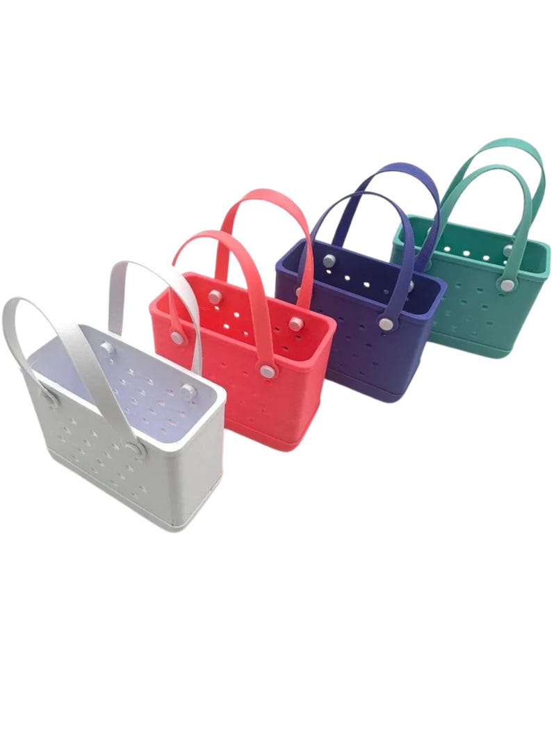 May include: Four brightly coloured tote bags. The bags are white, coral, purple, and teal. Each bag has a matching handle and is made of a solid material with small holes. The bags are rectangular in shape.