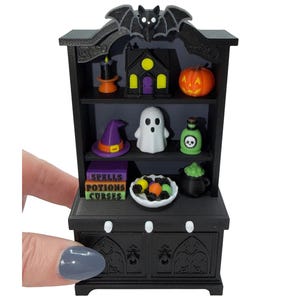 May include: A miniature black hutch featuring a bat topper and three shelves filled with Halloween-themed items including a candle, house, pumpkin, witch hat, ghost, potion bottle, books labeled Spells, Potions, Curses, and a cauldron.