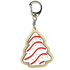 May include: A white and red Christmas tree cookie keychain with green sprinkles. The cookie is attached to a silver key ring.