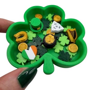 May include: A green shamrock-shaped tray filled with St. Patrick's Day themed miniatures. Includes gold coins, a leprechaun hat, a harp, a horseshoe, a pot of gold, and shamrock shapes. A heart with the Irish flag is also present.