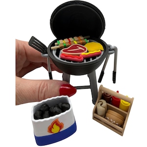 May include: Miniature black and gray barbecue grill with a variety of food items, including steak, hot dogs, and skewers. A small wooden caddy holds condiments. A container of charcoal and a spatula are also included.