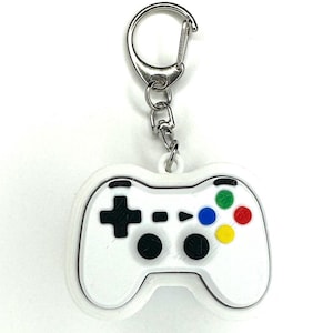 May include: White plastic video game controller keychain with a silver key ring. The controller has black buttons and a colorful button pad with red, green, blue, and yellow buttons.