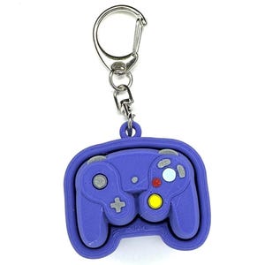 May include: Purple GameCube controller keychain with a silver key ring. The controller has a textured surface and features the iconic GameCube button layout.