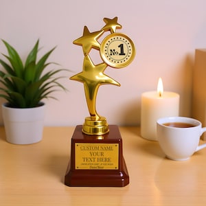 May include: A gold-colored trophy with a dark brown base. The trophy features three stars and a circular emblem with the number "No. 1". The base has a gold plaque with the text "CUSTOM NAME YOUR TEXT HERE".