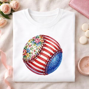 Puede incluir: Camiseta blanca con un diseño de béisbol. La pelota de béisbol tiene un estampado floral, rayas rojas y blancas y una sección de purpurina azul. El diseño está cosido con hilo rojo. La camiseta se muestra sobre una superficie blanca.