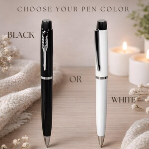 May include: Two ballpoint pens, one black and one white, each featuring a silver-toned clip and tip. The text CHOOSE YOUR PEN COLOR is at the top, with BLACK next to the black pen, OR in the center, and WHITE next to the white pen.