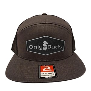 May include: A brown flat bill snapback hat with a black mesh back. The hat features a patch with the text "Only Dads" and a graphic of a beard and a hat. The Richardson brand tag is visible.