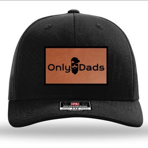 May include: Black trucker hat with a brown leather patch. The patch features the text "Only Dads" with a stylized beard and sunglasses graphic. The hat has a curved brim and a mesh back.