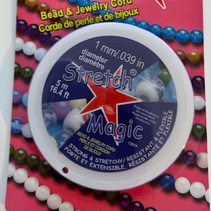 May include: A roll of clear stretch magic bead and jewelry cord. The cord is 1 mm in diameter and 16.4 feet long. The packaging is pink with a white circle in the center. The circle has a red star with the words "Stretch Magic" in blue letters. The packaging also has the words "Bead & Jewelry Cord" and "Corde de perle et de bijoux".