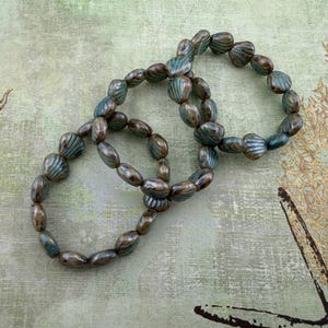 May include: Three beaded bracelets with a mix of teal and brown oval-shaped beads. The bracelets are arranged on a light green background with seashell and starfish illustrations.