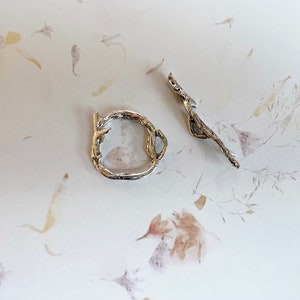 May include: Two silver rings with a textured, organic design. The rings are made to look like branches or twigs.