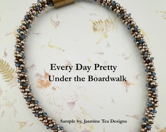 May include: A beaded necklace featuring a tubular design with metallic bronze and blue beads, secured by a cylindrical gold-tone magnetic clasp. The text Every Day Pretty Under the Boardwalk and Sample by, Jasmine Tea Designs is visible.