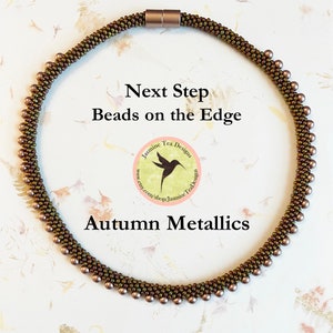 May include: A brown and gold beaded necklace with a magnetic clasp. The necklace is made with small seed beads and larger round beads. The necklace is labeled "Next Step Beads on the Edge" and "Autumn Metallics".