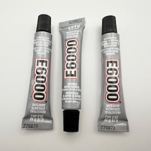 May include: Three tubes of E6000 industrial strength adhesive, each tube is 0.18 fl oz (5.3 ml) and has a black cap. The tubes are silver with black text and a warning label.