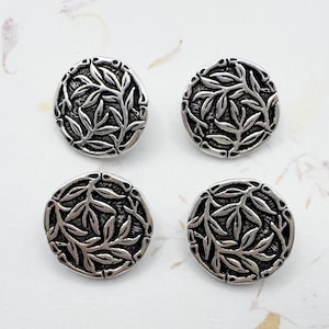 May include: Four silver-toned, round buttons with a detailed leaf design. The buttons are arranged in a square, showcasing their intricate, nature-inspired pattern. The buttons are made of metal.