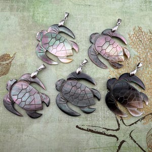 May include: Five sea turtle pendants crafted from iridescent shell material, each featuring a silver-toned metal bail at the top. The pendants display varying shades of dark gray, black, and pearlescent tones with etched geometric shell patterns.