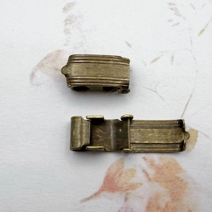 May include: Two antique gold-toned metal clasps for jewelry making. One clasp is a simple rectangular shape, the other is a hinged clasp with a decorative edge.