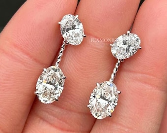 May include: A pair of dangling earrings featuring two oval-cut gemstones each. The gemstones are connected by a twisted silver-colored metal. The earrings are displayed against a blurred background.