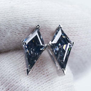 May include: A pair of kite-shaped, gray gemstone earrings with silver metal settings. The gemstones have multiple facets, reflecting light. The earrings are displayed on a white surface. The brand name "FEXMON JEWELS" is visible.