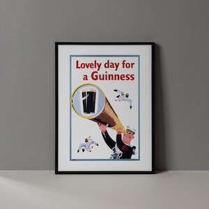 Op de afbeelding: Een ingelijste vintage poster met de tekst "Lovely day for a Guinness". De poster toont een cartoonmatroos die door een telescoop naar een pint Guinness kijkt, met meeuwen die rondvliegen.