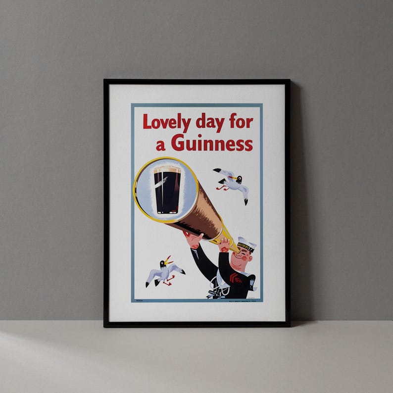 Op de afbeelding: Een ingelijste vintage poster met de tekst "Lovely day for a Guinness". De poster toont een cartoonmatroos die door een telescoop naar een pint Guinness kijkt, met meeuwen die rondvliegen.