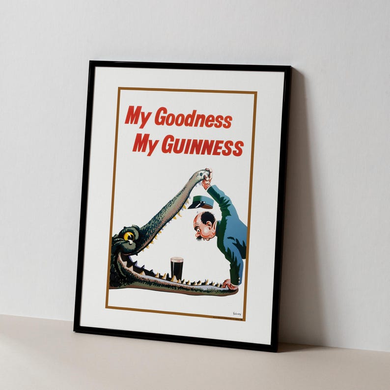 May include: Framed vintage advertisement poster with the text "My Goodness My Guinness" in red. The illustration depicts a man and a crocodile with a pint of Guinness. The poster is in a black frame.