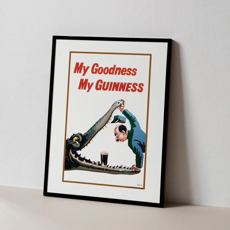Op de afbeelding: Ingelijste vintage Guinness-advertentieposter met de tekst "My Goodness My Guinness" in het rood. De illustratie toont een man en een krokodil met een pint Guinness. De poster zit in een zwart frame.