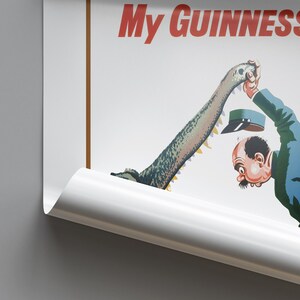 Op de afbeelding: Vintage Guinness-advertentieposter met een cartoonillustratie van een man en een krokodil. De woorden "My Guinness" staan in het rood. De poster heeft een witte achtergrond en is gedeeltelijk opgerold.