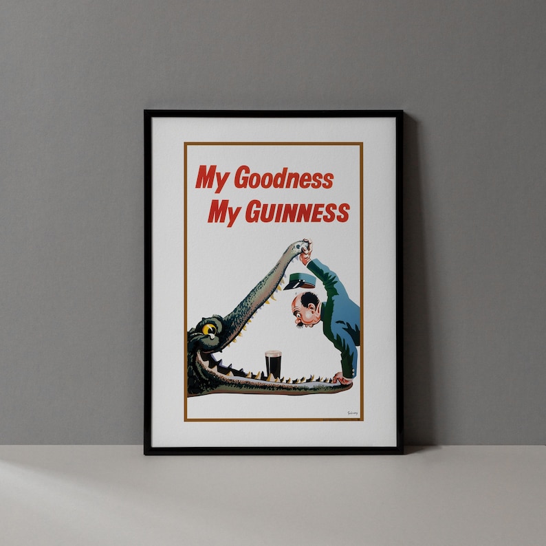 Op de afbeelding: Ingelijste vintage advertentieposter met de tekst "My Goodness My Guinness" in het rood. De afbeelding toont een man in een blauw pak en een krokodil met een pint Guinness. De poster zit in een zwart frame.