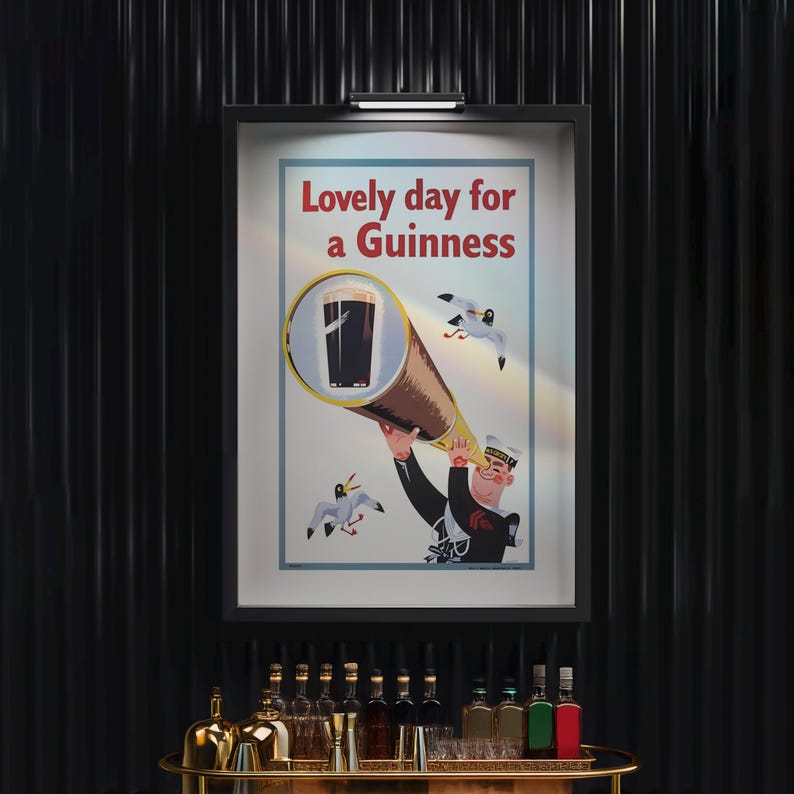 May include: A framed vintage advertisement for Guinness stout. The poster features a sailor looking through a telescope at a pint of Guinness, with the text "Lovely day for a Guinness" in red. Two seagulls are flying in the background.
