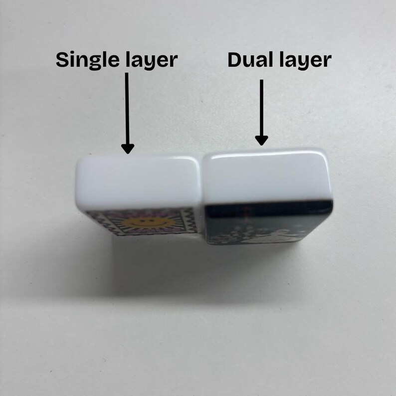 Puede incluir: Dos fichas rectangulares con lados blancos y reverso negro, colocadas una al lado de la otra. La ficha izquierda est&aacute; etiquetada como Single layer con una flecha, y la derecha como Dual layer con una flecha. La ficha izquierda tiene un sol amarillo.