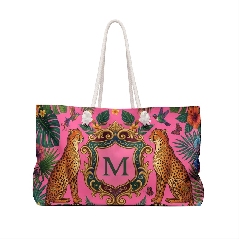 May include: A large pink tote bag with a white rope handle. The bag features a cheetah design with a floral and foliage pattern. The center has a pink crest with the letter "M".