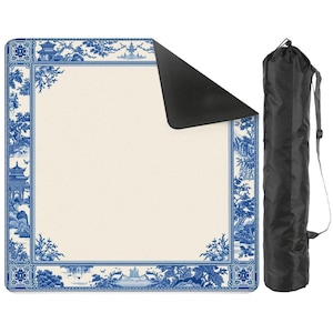May include: A square picnic blanket with a cream-colored center and a blue and white Chinoiserie border design. A black carrying bag with a shoulder strap is next to the blanket. The blanket is folded with a black underside visible.